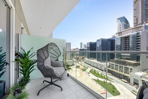 A balcony with a modern chair, potted plants, and a city view. - Luxury 1BR, Business Bay, Burj Khalifa Peek View (Dubai)
