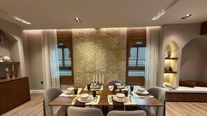 A dining area with a stone accent wall, a wooden table set for four, and a seating arrangement with chairs. - Atrah Luminous 3BR Luxury Family Residence (Madinah)