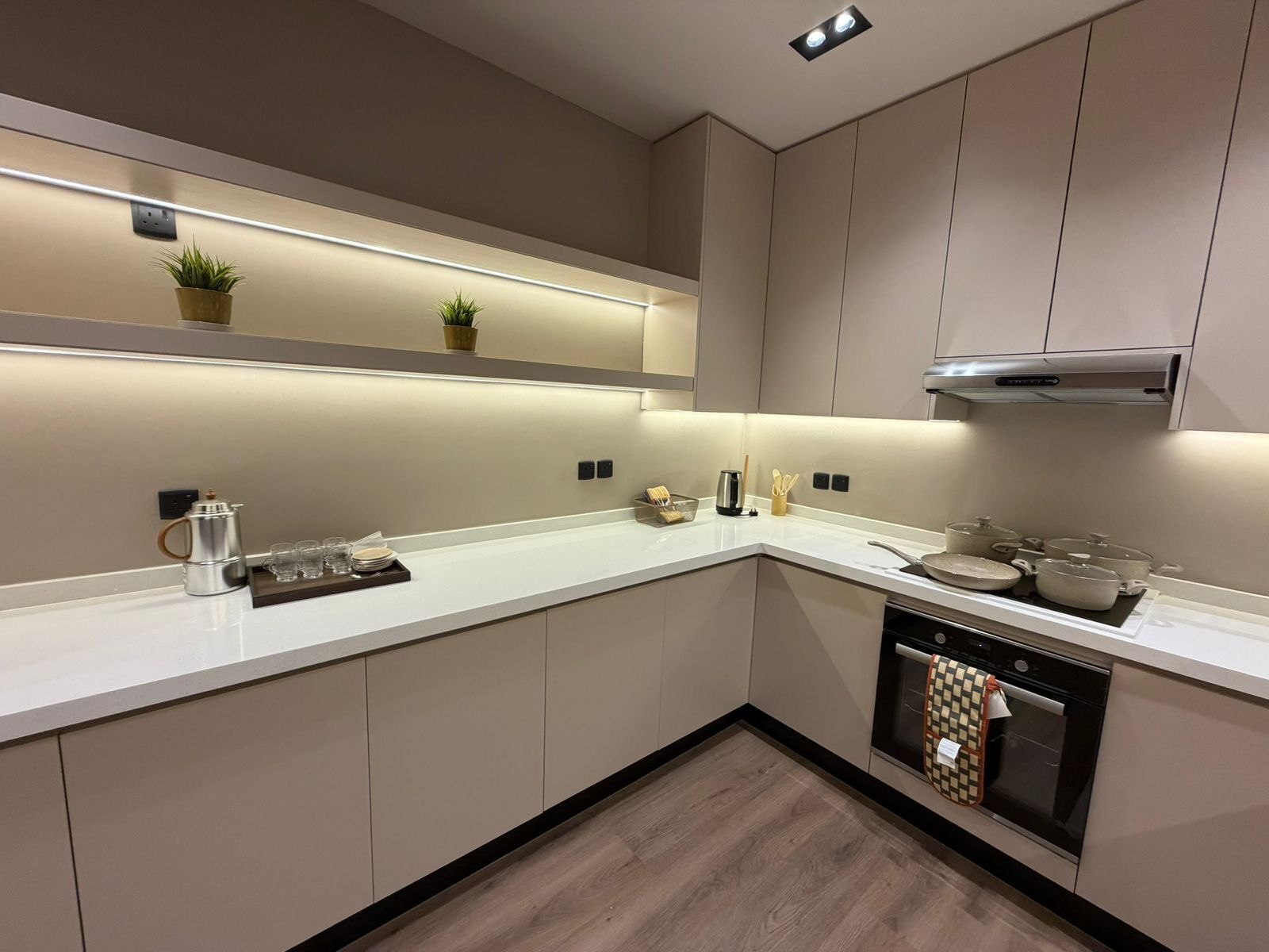 Une cuisine moderne avec un plan de travail blanc, des appareils en acier inoxydable et un revêtement de sol en bois.