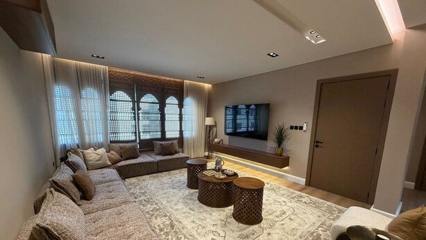 A modern living room with a sectional sofa, a flat-screen TV, a coffee table, and a patterned rug.