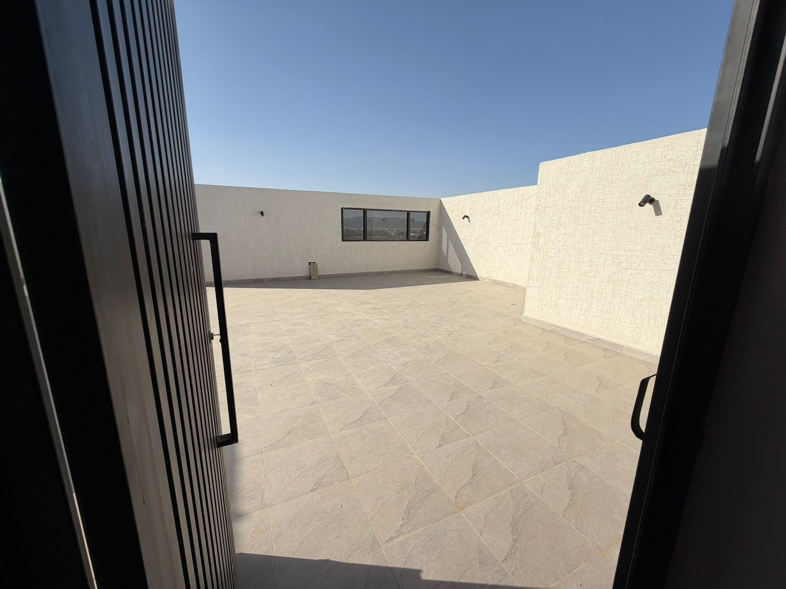 Une terrasse ouverte avec un sol carrelé, une fenêtre et une porte.