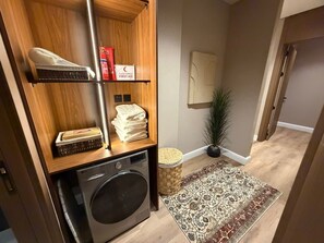 Un espace buanderie comprenant un lave-linge LG, une étagère avec une paire de chaussures, une trousse de premiers secours et un panier en osier.