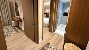 A hotel room with a wooden floor, a bed, a bathroom with a shower, and a TV mounted on the wall.
