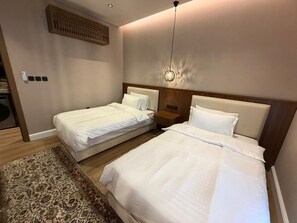 Een hotelkamer met twee bedden, een houten hoofdbord, een hanglamp en een kamerkleed met dessin.