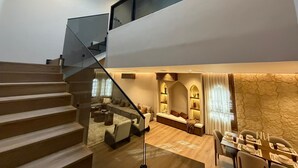 Ein modernes Interieur mit einer Treppe, einem Wohnbereich inklusive Sofa und Couchtisch sowie einem Essbereich mit Tisch für vier Personen.