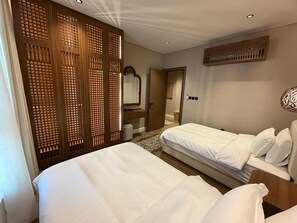 A hotel room with two beds, a wooden partition, a mirror, and a ceiling vent. - Atrah Sophisticated 3BR Family Sanctuary (Madinah)