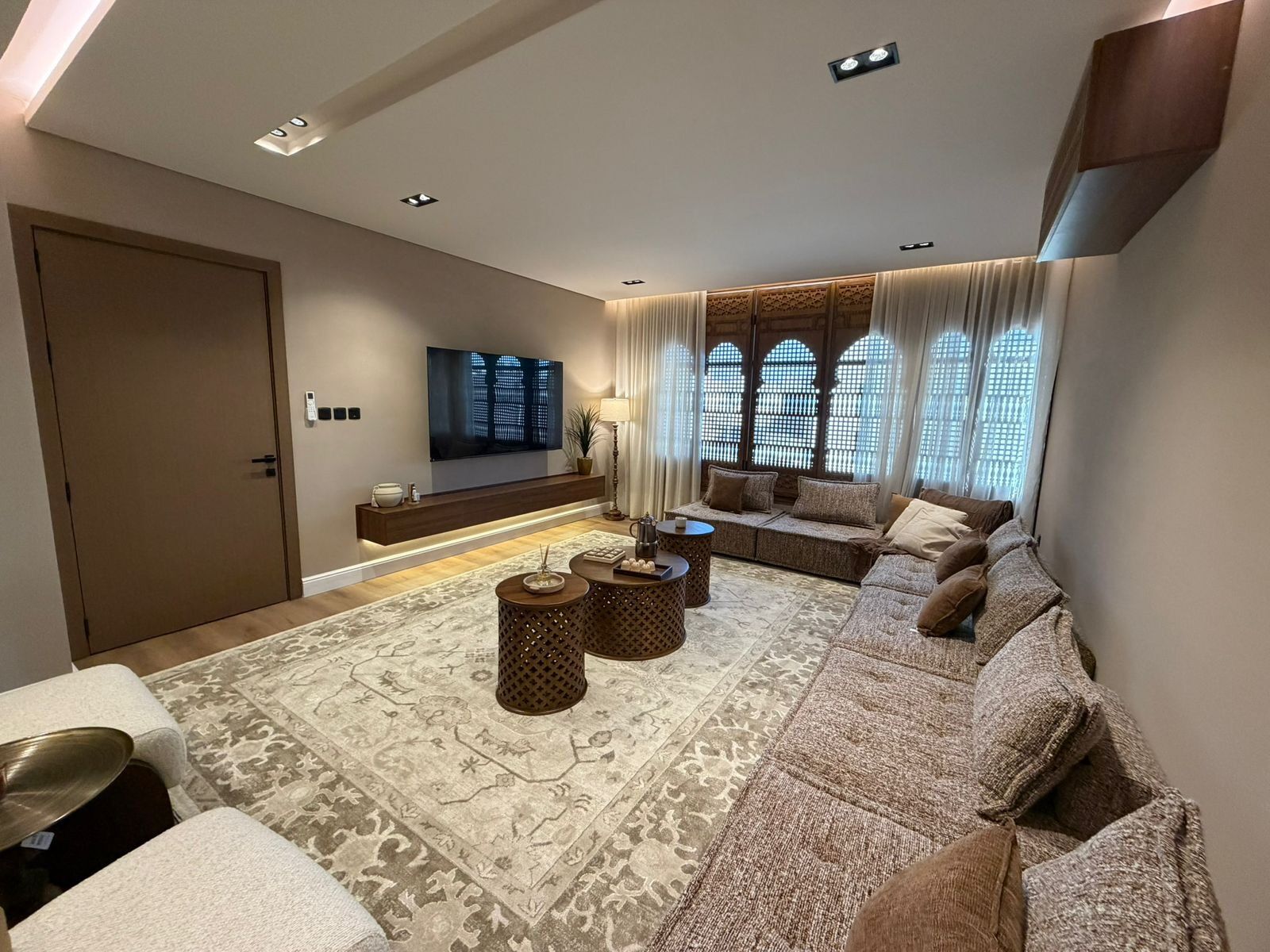 A modern living room with a sofa set, a flat-screen TV, a coffee table, and patterned rugs.
