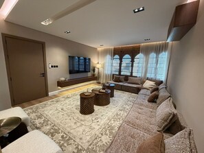 A modern living room with a sofa set, a flat-screen TV, a coffee table, and patterned rugs. - Atrah Sophisticated 3BR Family Sanctuary (Madinah)