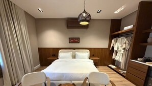 Habitación de hotel con una cama grande, dos mesitas de noche, un armario, una zona de estar con una pequeña mesa y un adorno en la pared.