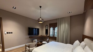 Una habitación de hotel moderna con una cama grande, un escritorio con silla, un televisor y una ventana con cortinas.