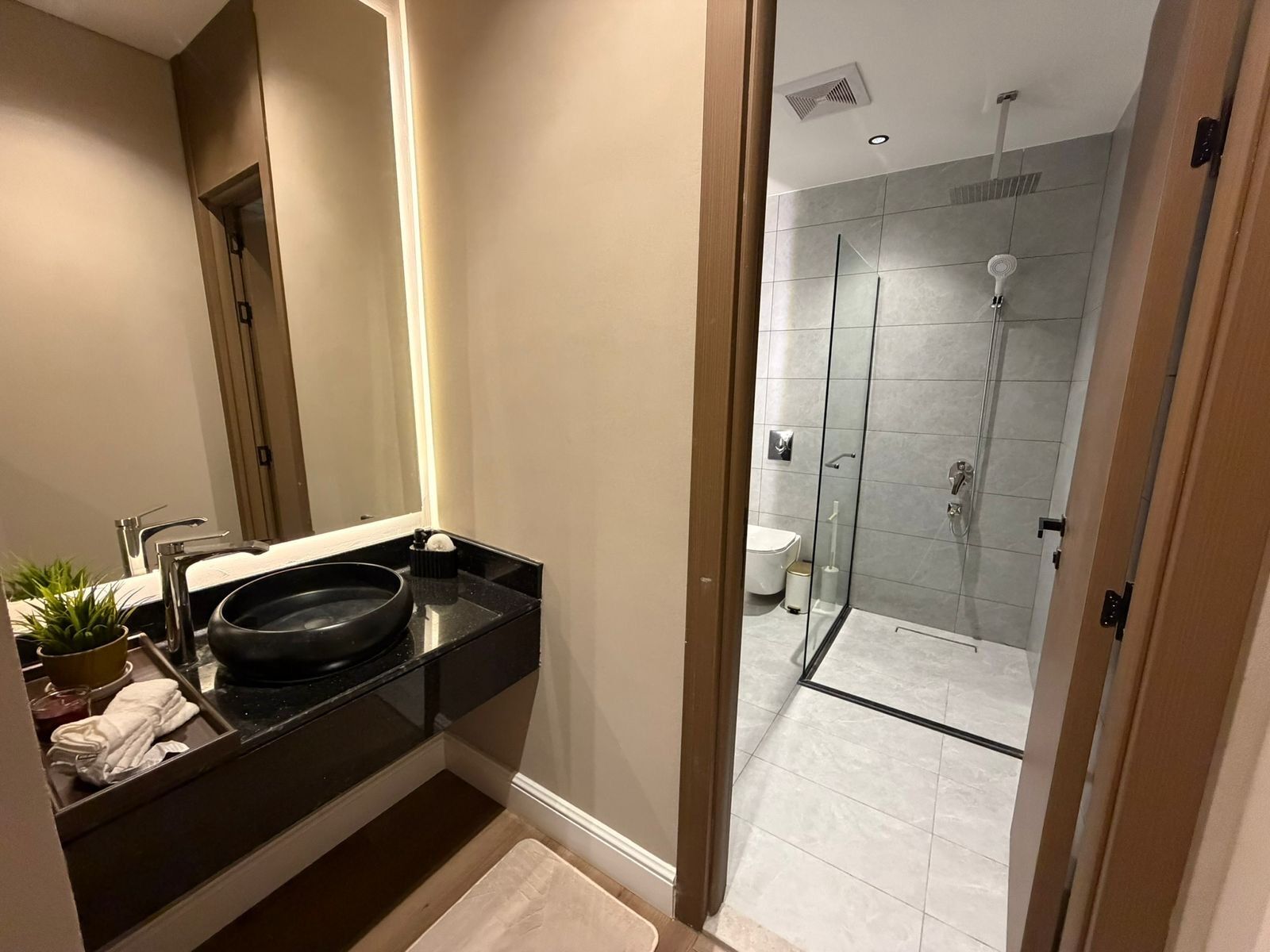 Un baño moderno con lavamanos negro, espejo y cabina de ducha de vidrio.