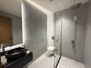 Um banheiro moderno com chuveiro envidraçado, pia preta e vaso sanitário.