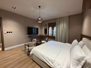 Quarto de hotel com cama, escrivaninha, cadeira, televisão e janela com cortinas.
