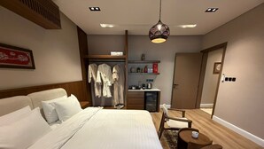Una habitación de hotel con una cama grande, un escritorio con computadora, un armario y una bata colgada.