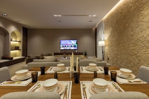 A modern living room with a flat-screen TV, sofas, a dining table set for four, and a stone accent wall. - Atrah Elegant 3BR Apartment With Maid's Room (Madinah)