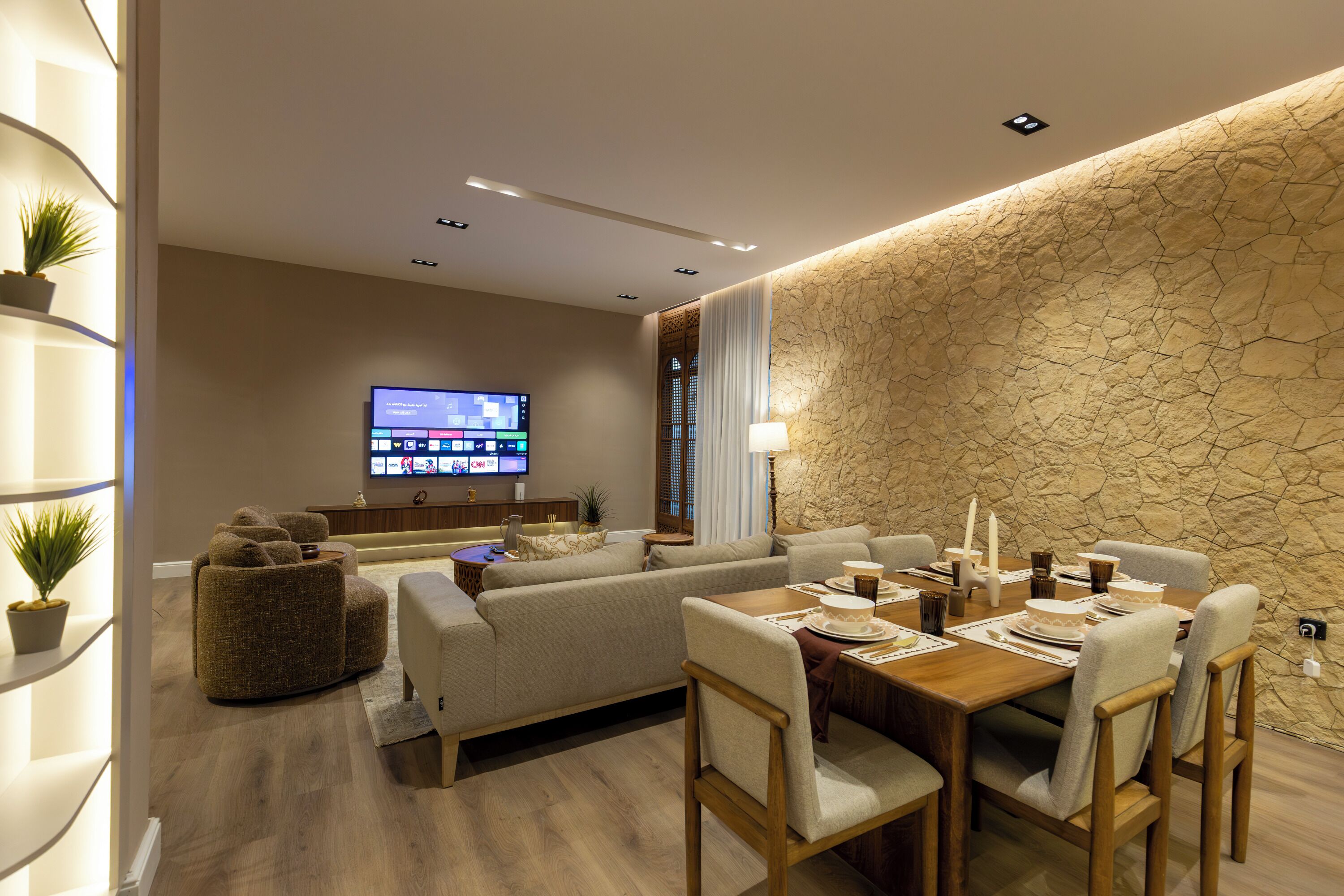 Un salon moderne comprenant un canapé, une table à manger, des chaises, un téléviseur à écran plat et un mur décoratif en pierre.