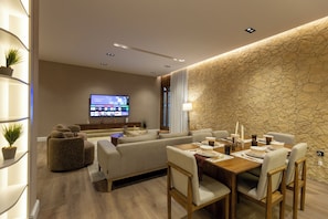 Uma sala de estar moderna com sofá, mesa de jantar, cadeiras, televisão de tela plana e uma parede de destaque em pedra.