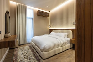 A modern bedroom with a large bed, a bedside table, a nightstand, a wall-mounted air conditioner, and a patterned rug. - Atrah Elegant 3BR Apartment With Maid's Room (Madinah)