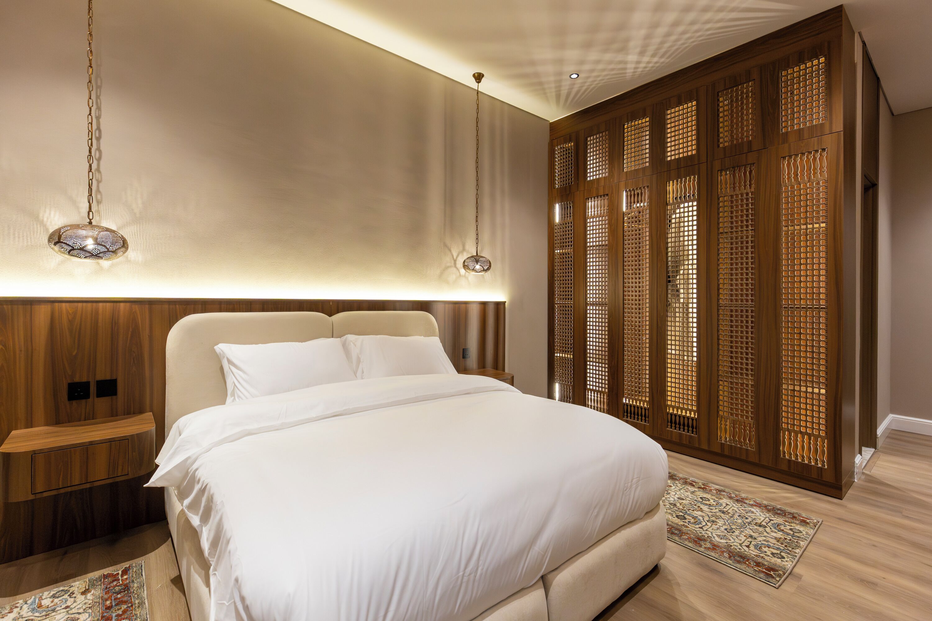 A bedroom with a large bed, wooden headboard, bedside tables, and a decorative wall panel.