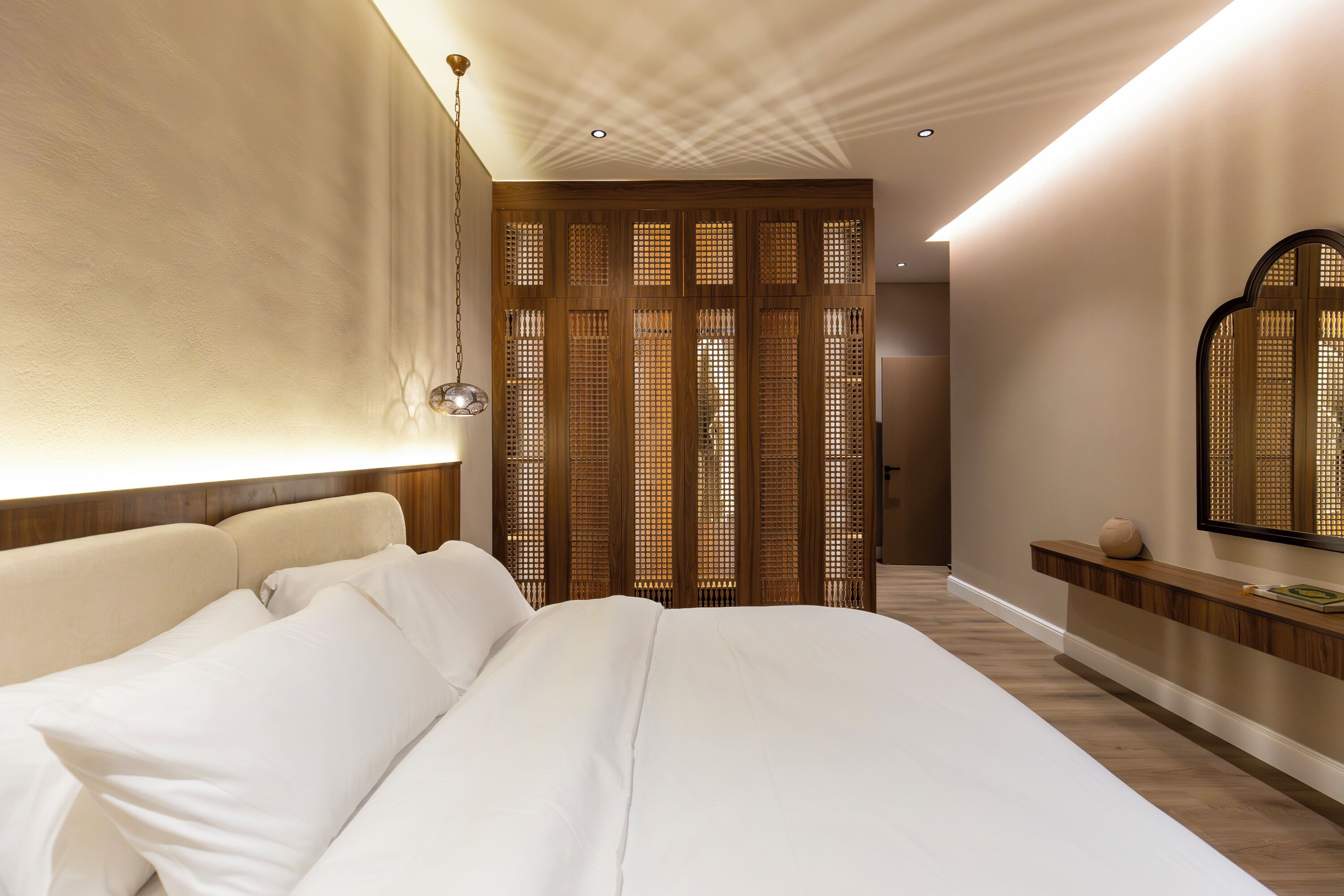 Une chambre d’hôtel moderne avec un grand lit, une cloison en bois et un miroir fixé au mur.