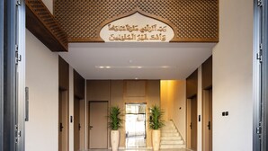 A hotel lobby with a modern design, featuring a central staircase, two large potted plants, and a decorative ceiling. - Atrah Tranquil Studio Near Al Masjid An Nabawi (Madinah)