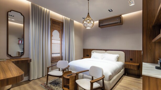 A modern bedroom with a large bed, two chairs, a wooden desk, a mirror, and a decorative hanging light fixture. - Atrah Tranquil Studio Near Al Masjid An Nabawi (Madinah)