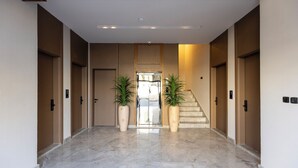A modern hotel lobby with a marble floor, two large potted plants, a staircase, and a patterned ceiling. - Atrah Tranquil Studio Near Al Masjid An Nabawi (Madinah)