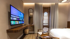 A hotel room with a flat-screen TV mounted on the wall, a bed, a desk with a chair, and a window with curtains. - Atrah Tranquil Studio Near Al Masjid An Nabawi (Madinah)