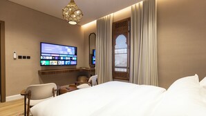 A hotel room with a large bed, a flat-screen TV mounted on the wall, a desk with a chair, and a decorative window with curtains. - Atrah Tranquil Studio Near Al Masjid An Nabawi (Madinah)