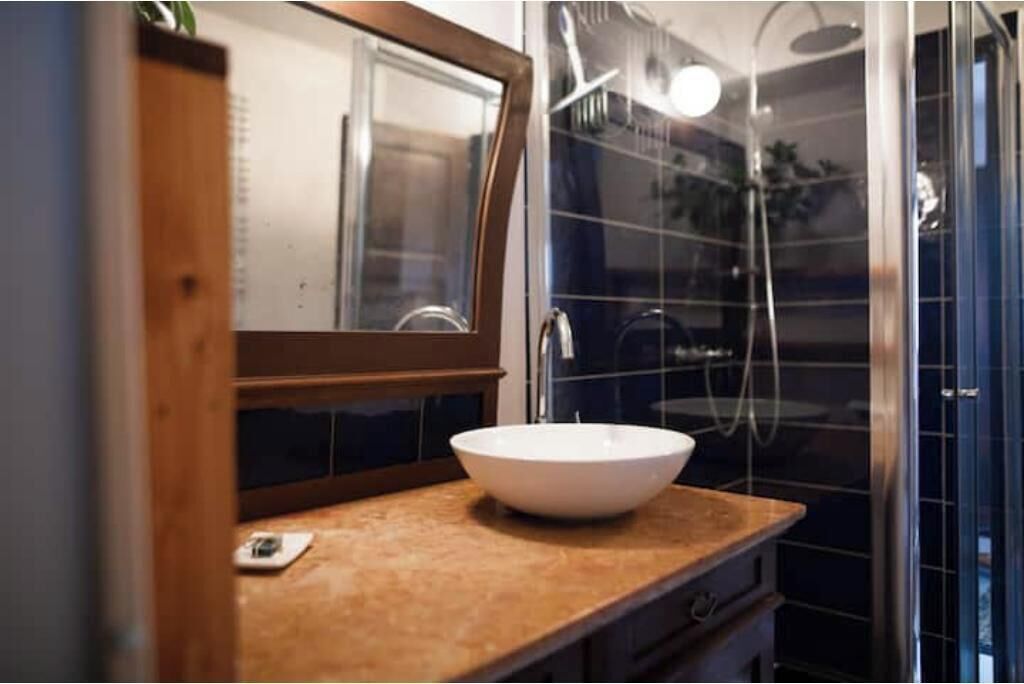 Ein Badezimmer mit weißem Waschbecken, einem Holz-Waschtisch, einem Spiegel und einer Duschkabine aus Glas.