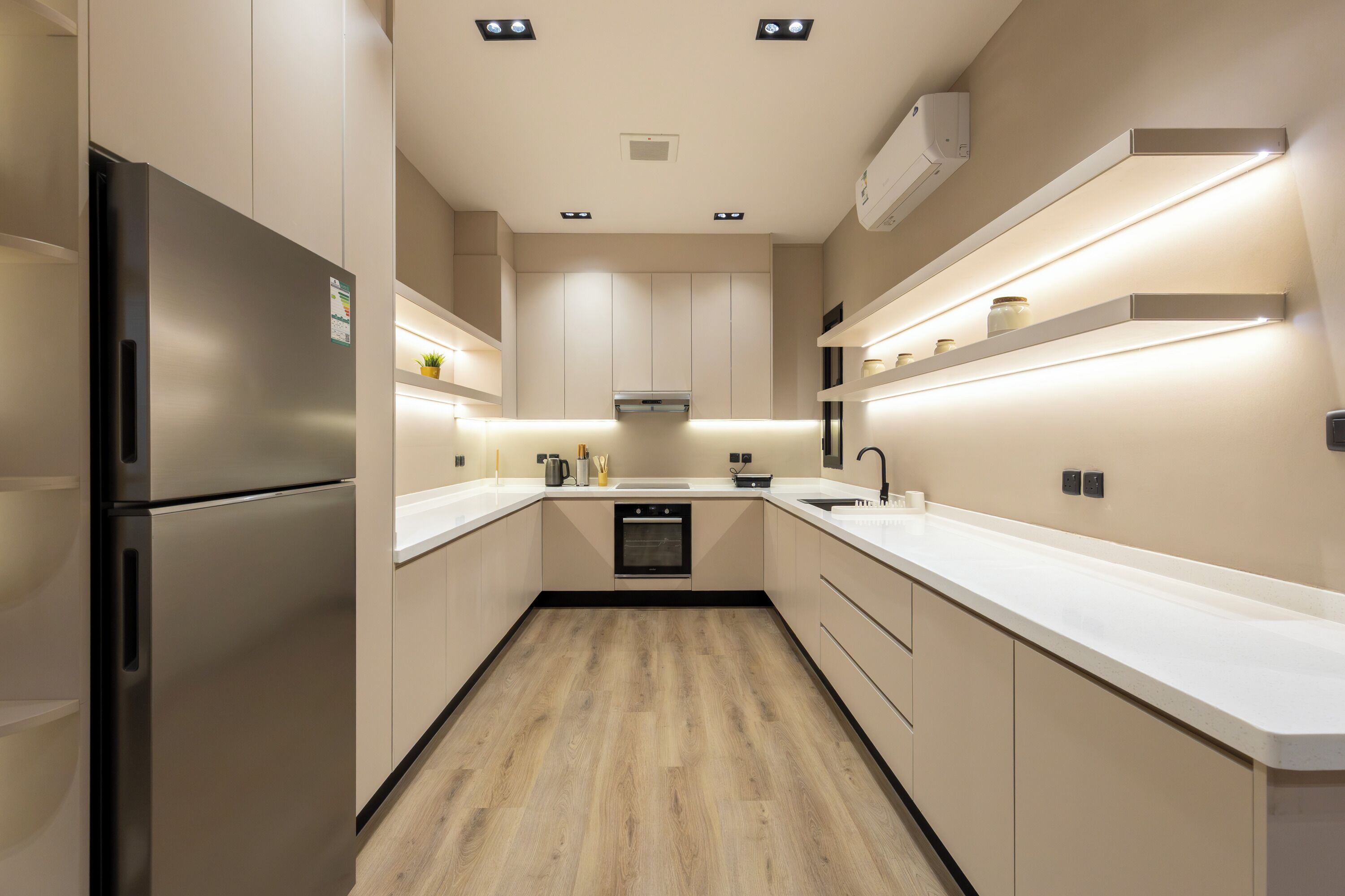Une cuisine moderne dotée d’un réfrigérateur en acier inoxydable, de meubles blancs, d’un îlot central et d’un éclairage sous les meubles.