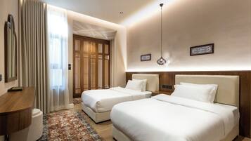 Une chambre d’hôtel avec deux lits, une tête de lit en bois, une table de chevet, une petite table d’appoint, un luminaire suspendu et un tapis à motifs.