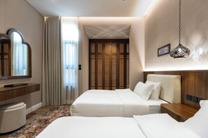 A hotel room with two beds, a wooden headboard, a nightstand, a mirror, a wooden door with a lattice design, and a patterned rug.