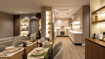 A modern dining area with a long table set for a meal, a kitchen in the background, and a seating area with a sofa.