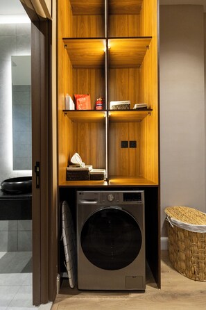 A laundry room with a washing machine, shelves with items, and a basket. - Atrah Spacious 3BR Family Stay + Maid's Room (Madinah)