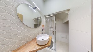 Ein Badezimmer mit einem runden Waschbecken, einem Spiegel und einer Dusche.