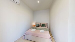 Ein kleines, modernes Schlafzimmer mit Bett, Nachttischlampe und Klimaanlage.