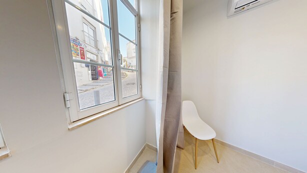 Ein Zimmer mit Fenster, einem weißen Stuhl und einem Vorhang.