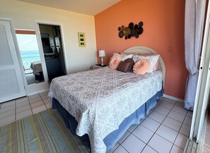 A bedroom with a bed, a nightstand, a lamp, a view of the ocean through a door, and a wall with decorative items. - The Pink Turtle-New Booking Discount-Gorgeous Sea Views, Generator, Wifi, Pool (Christiansted)