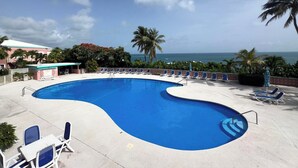 En pool med solstolar, utsikt över havet och palmer.