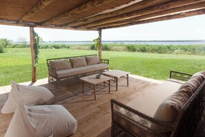 A covered outdoor seating area with a sofa, chairs, and a table, overlooking a grassy field and water. - Little Papyrus Cottage (Toscana)