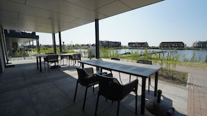 Eine Terrasse im Freien mit Tischen und Stühlen, mit Blick auf ein Gewässer und Gebäude.
