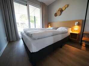 A hotel room with a bed, a nightstand, a wall-mounted light, and a window with curtains. - Water-view Holiday Home in Kampen (Kampen)