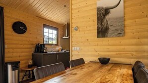 A wooden cabin interior with a dining table, chairs, a clock, a kitchen area, and a bull's head artwork. - Holiday Home in Otterlo With Terrace (Otterlo)