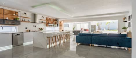 A modern kitchen with a central island, bar stools, and a blue sofa in a spacious living area with a view.