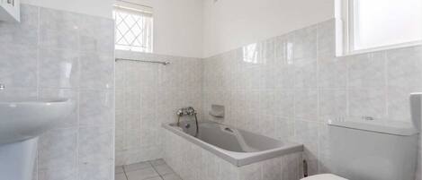 A bathroom with a bathtub, toilet, and sink, tiled in a light color.