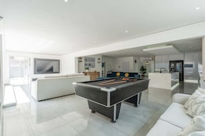 A modern living room with a pool table, a sofa, a TV, and a kitchen area. - Morden Stylish Villa (uMhlanga)
