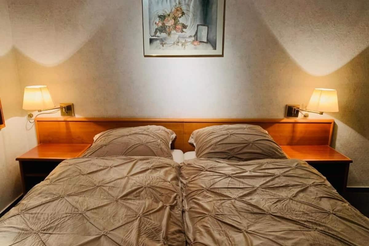 A bed with a quilted cover, two bedside lamps, and a framed picture on the wall.
