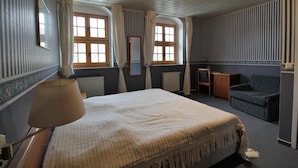 Una habitación de hotel con una cama, una silla, una mesa y un ventanal con cortinas.