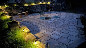 Un patio empedrado con paredes de piedra, un banco de madera, una mesa de metal y sillas.